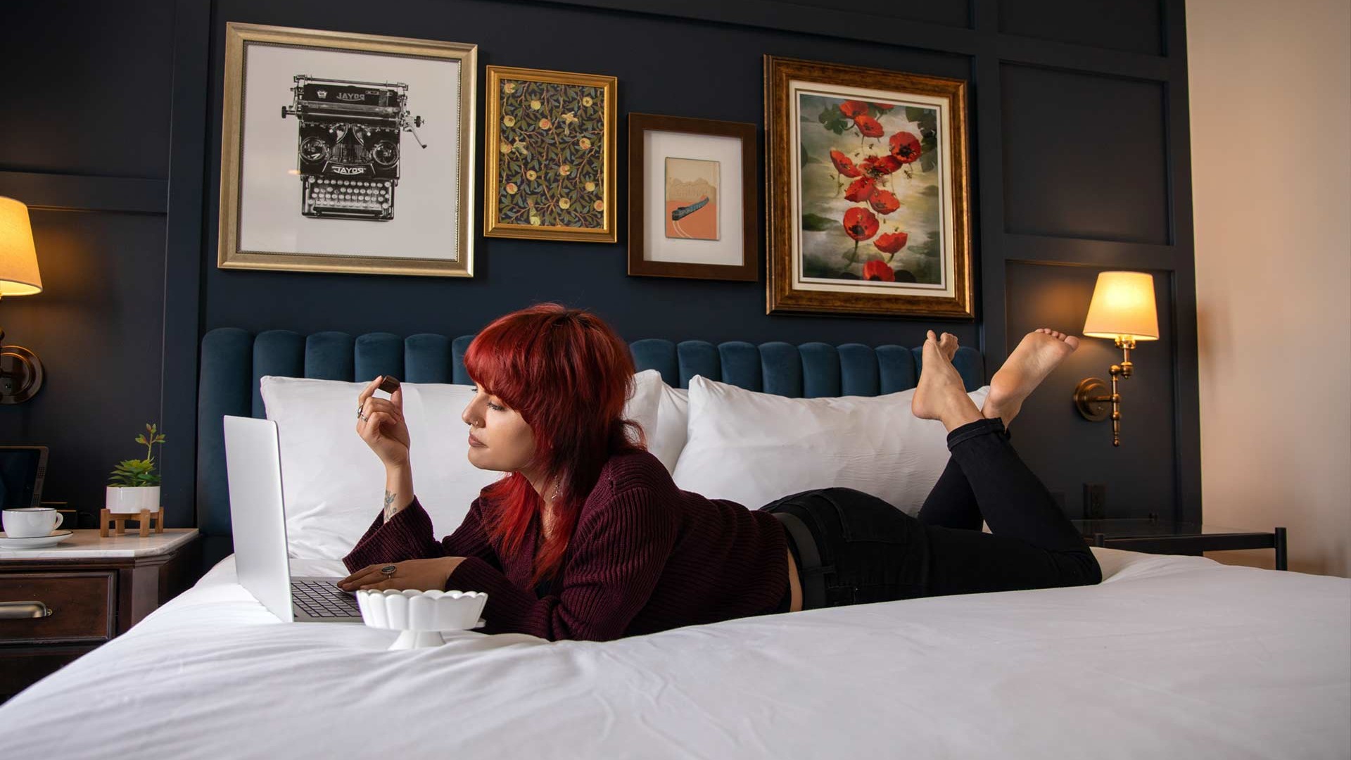 A woman lying in bed, typing at her laptop while enjoying a piece of Nove luxury chocolates.