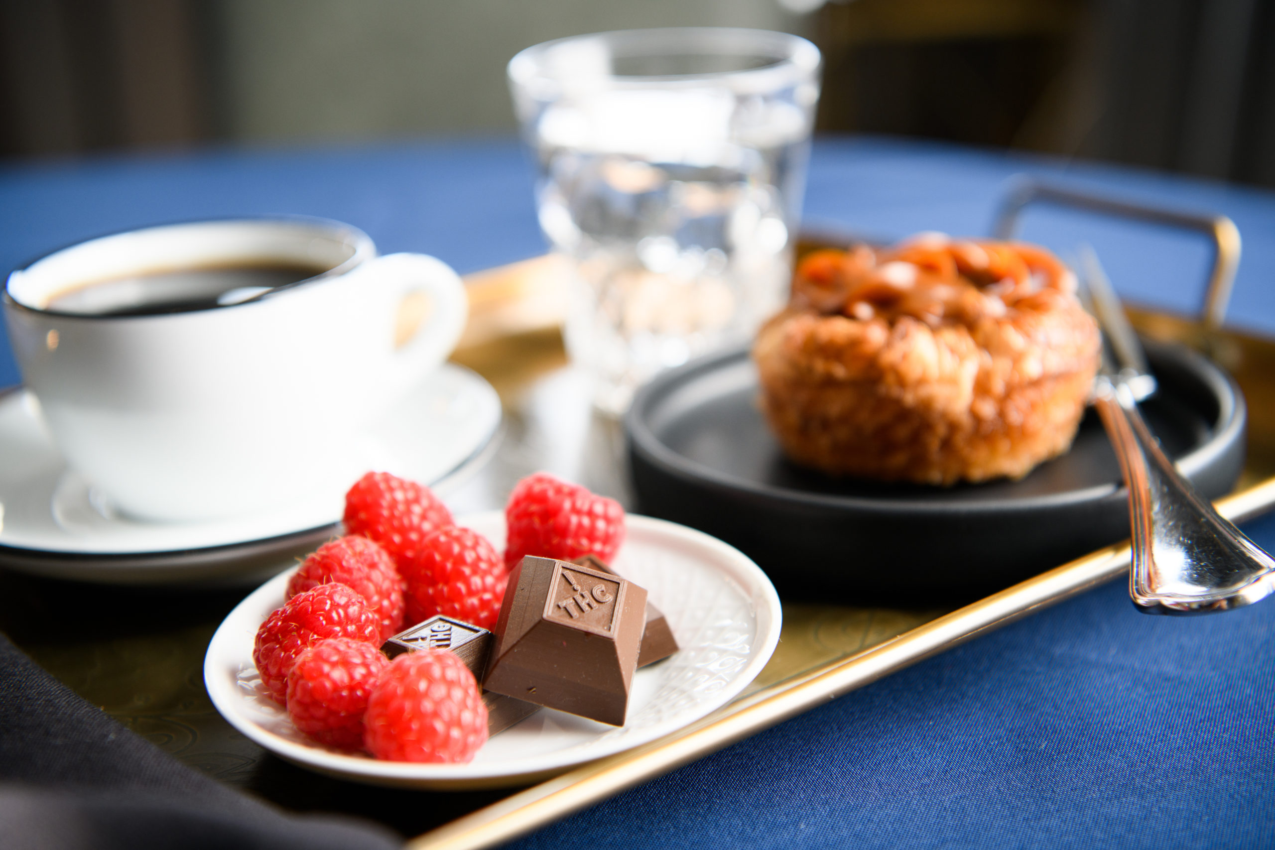 Nove cannabis-infused luxury chocolates resting on a small plate with raspberries; the plate rests on a breakfast tray. Discover your edible ritual.