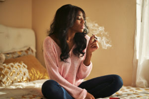 african american woman smoking marijuana joint while sitting on bed at home