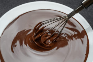 Macro of Melted milk or dark chocolate swirl in plate and whisk on dark concrete background