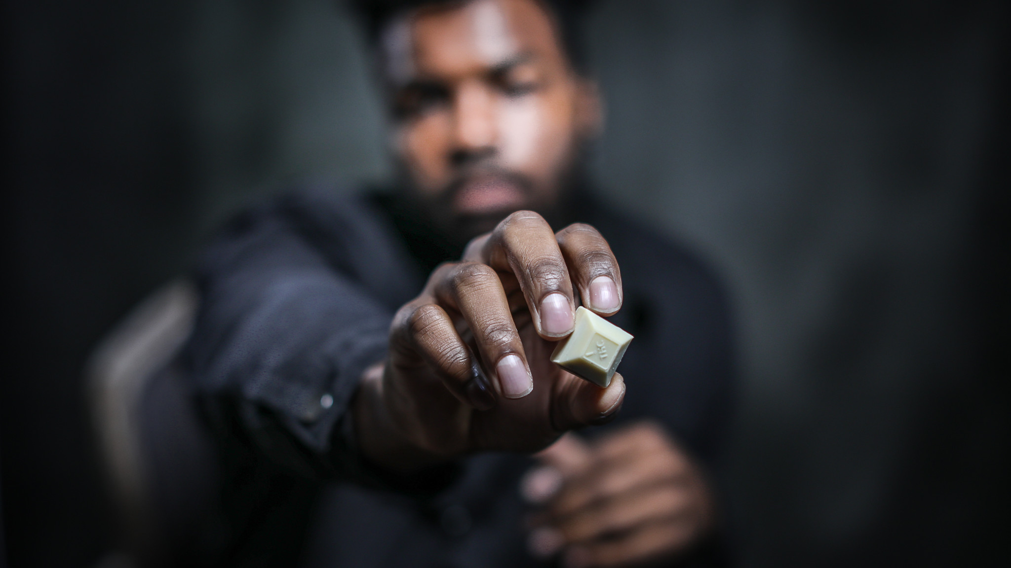 A young black man holding a piece of Nove Cafe Cappuccino cannabis-infused chocolate up close to the camera.