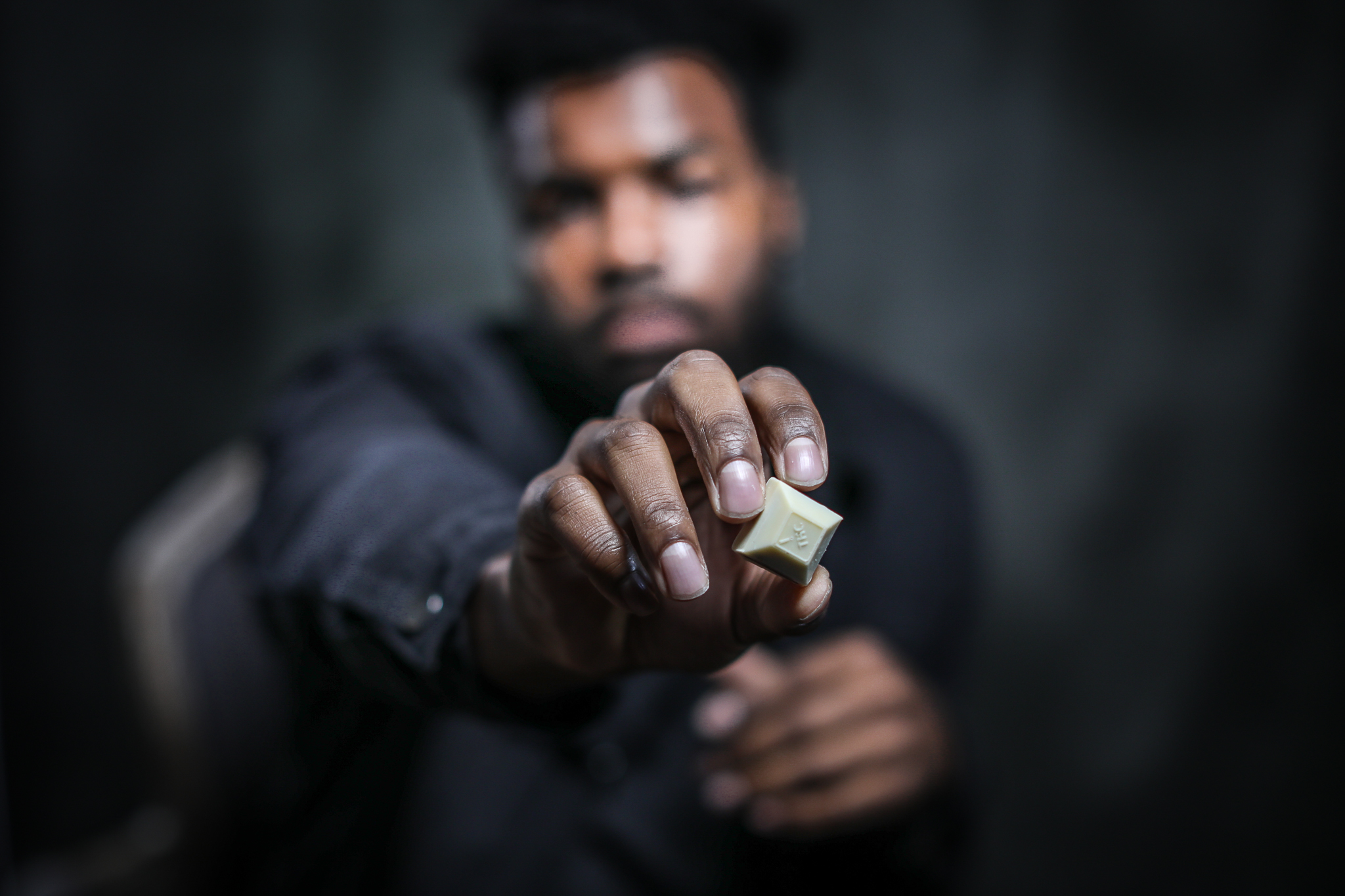 A young black man holding a piece of Nove Cafe Cappuccino cannabis-infused chocolate up close to the camera.