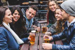 Group of friends enjoying a beer at pub in London, toasting and laughing. Four girls and two boys in their twenties having fun together. Friendship and lifestyle concepts