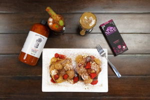 Flatlay composition.  French toast topped with cannabis-infused dalgona coffee cream rests on a table with Dead Veggies Bloody Matty mix and Nove Raspberry Bramble.