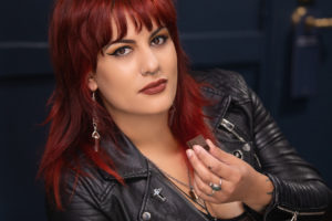 A woman with red hair and a leather jacket eating a piece of Nove Luxury Chocolates.  Pair beer and cannabis for the ultimate experience.