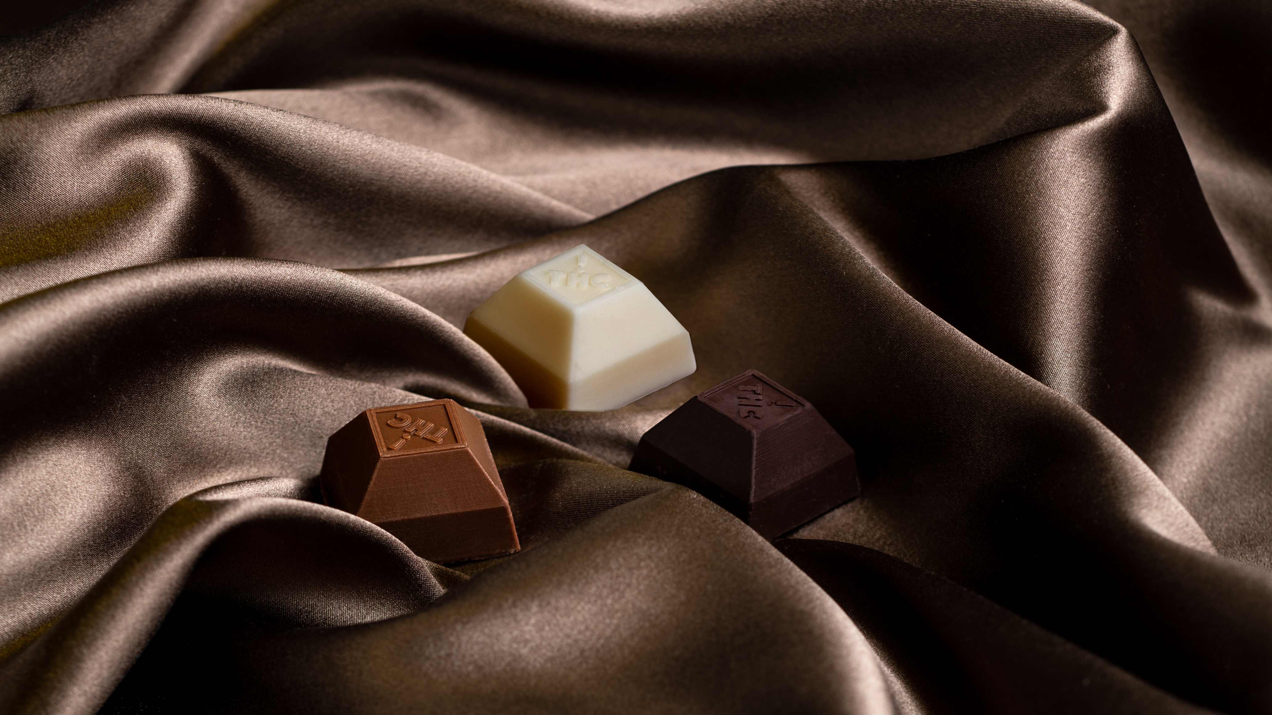 Three squares of milk, white, and dark chocolate from Nove, resting on silk.