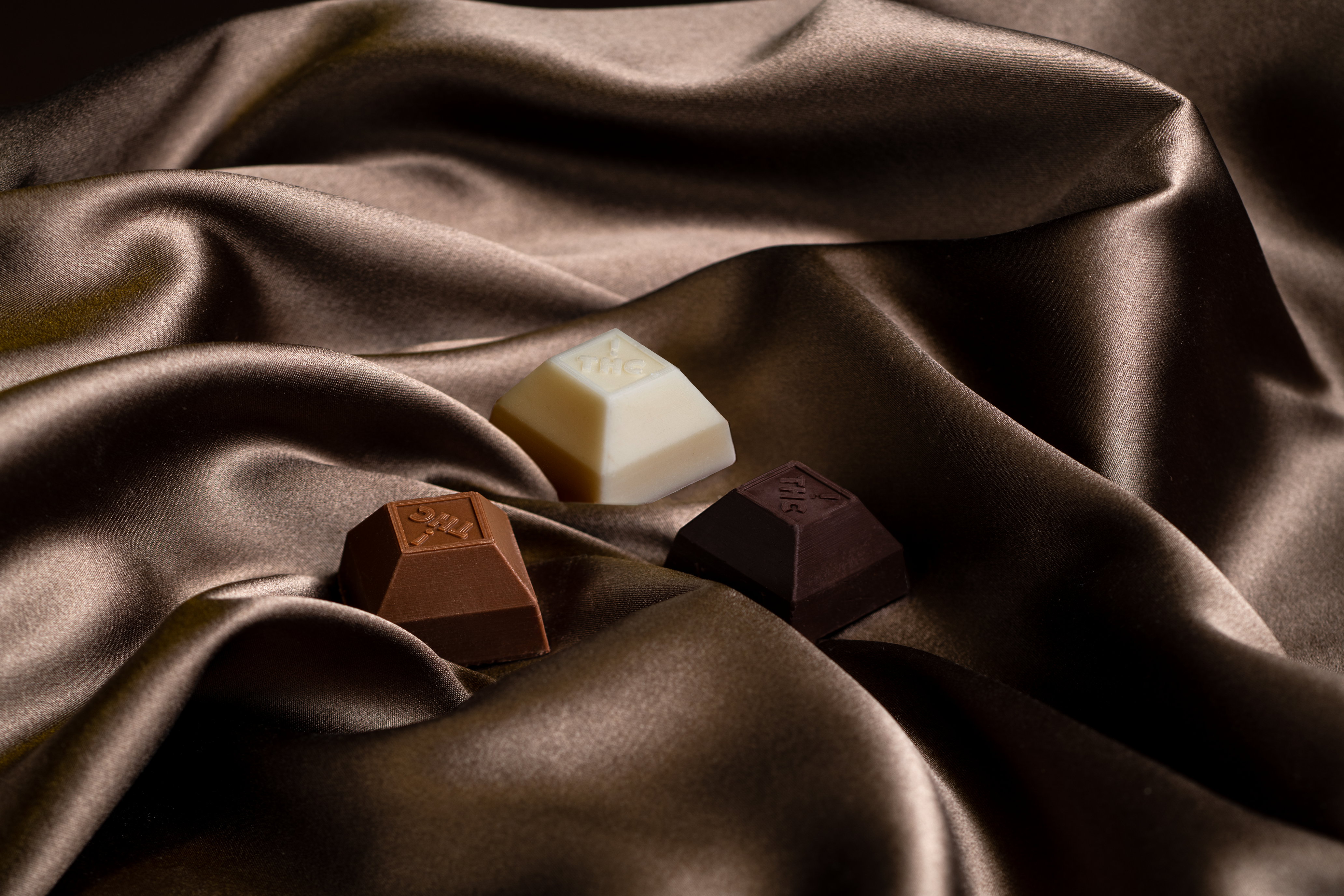 Three squares of milk, white, and dark chocolate from Nove, resting on silk.
