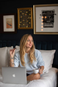 A woman sitting on a bed with a laptop and cup of coffee, consuming cannabis chocolate edibles.